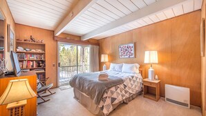 A bedroom with a large bed, a bookshelf, a desk with a lamp, and a view of the outdoors. - Mahogany by Avantstay Snowbird Cabin w Full Chamberlands Access (Homewood)