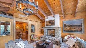 A spacious living room with a stone fireplace, wooden beams, and a large painting on the wall. - Mahogany by Avantstay Snowbird Cabin w Full Chamberlands Access (Homewood)