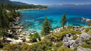 A coastal landscape with clear turquoise waters, rocky shores, and dense pine forests. - Mahogany by Avantstay Snowbird Cabin w Full Chamberlands Access (Homewood)