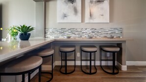 Une cuisine moderne avec un coin bar, deux tabourets, une plante en pot et des œuvres d’art abstraites accrochées au mur.