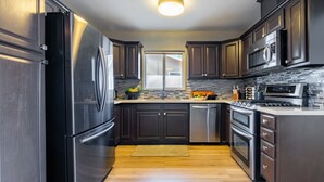 Une cuisine moderne avec des meubles de couleur sombre, des appareils en acier inoxydable, un dosseret carrelé et un îlot central.