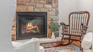 A stone fireplace with a fire, a wooden rocking chair, and a patterned rug.