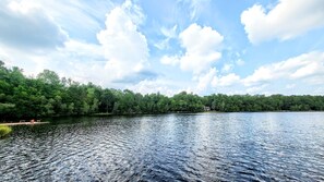 Un lago tranquilo con un muelle y árboles al fondo.