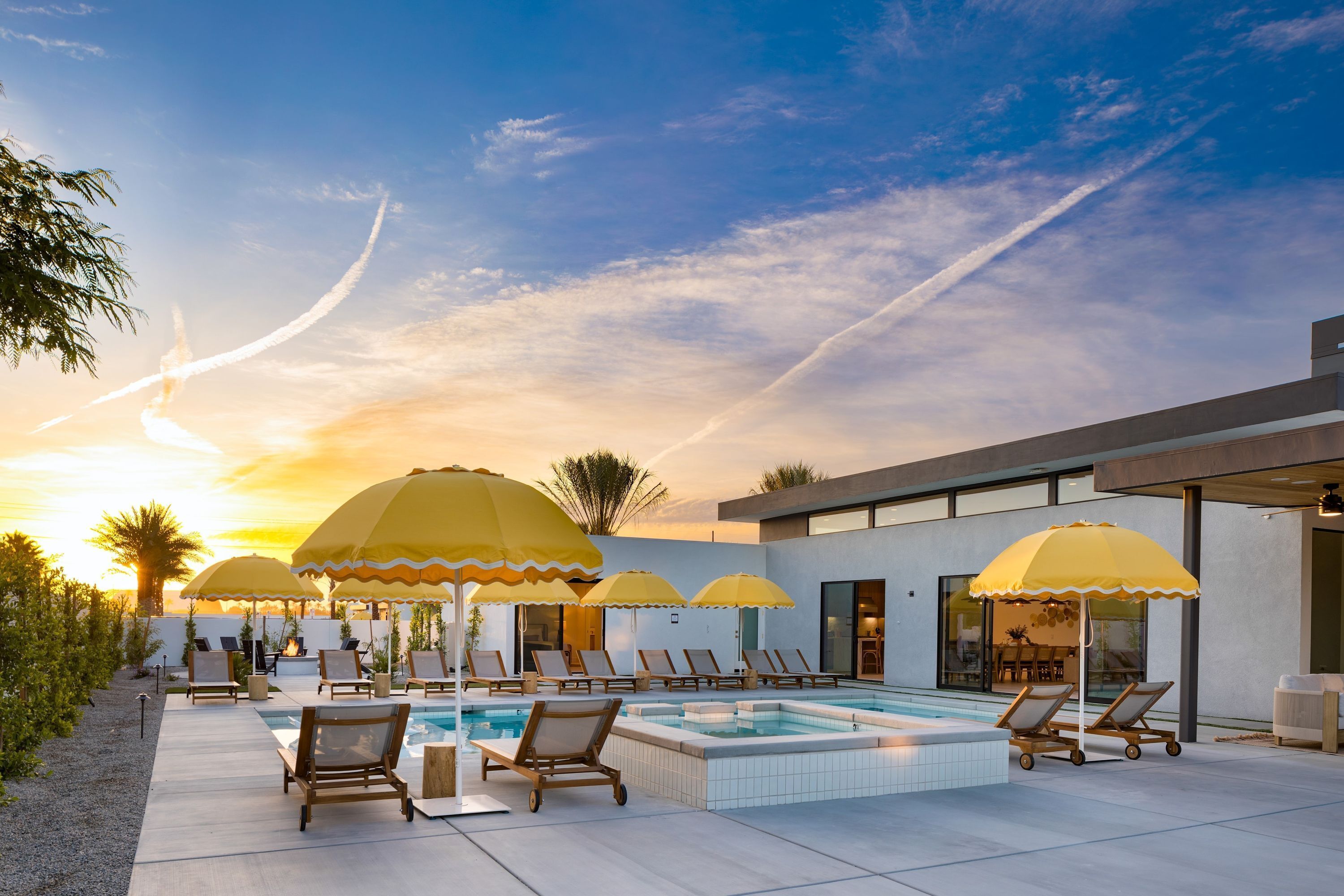 Un espace aménagé au bord de la piscine, avec des chaises longues et des parasols, un jacuzzi, et un bâtiment moderne en arrière-plan.