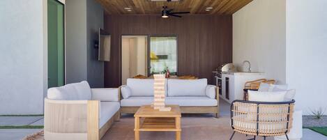 A modern outdoor seating area with a wooden ceiling, a ceiling fan, and a wooden coffee table.
