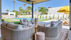 A modern outdoor living area with a pool, seating, and a view of the backyard.