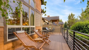 Une terrasse en bois avec des chaises longues, un barbecue et un espace patio couvert.