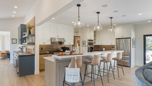 A modern kitchen with a central island, bar stools, pendant lighting, and stainless steel appliances.