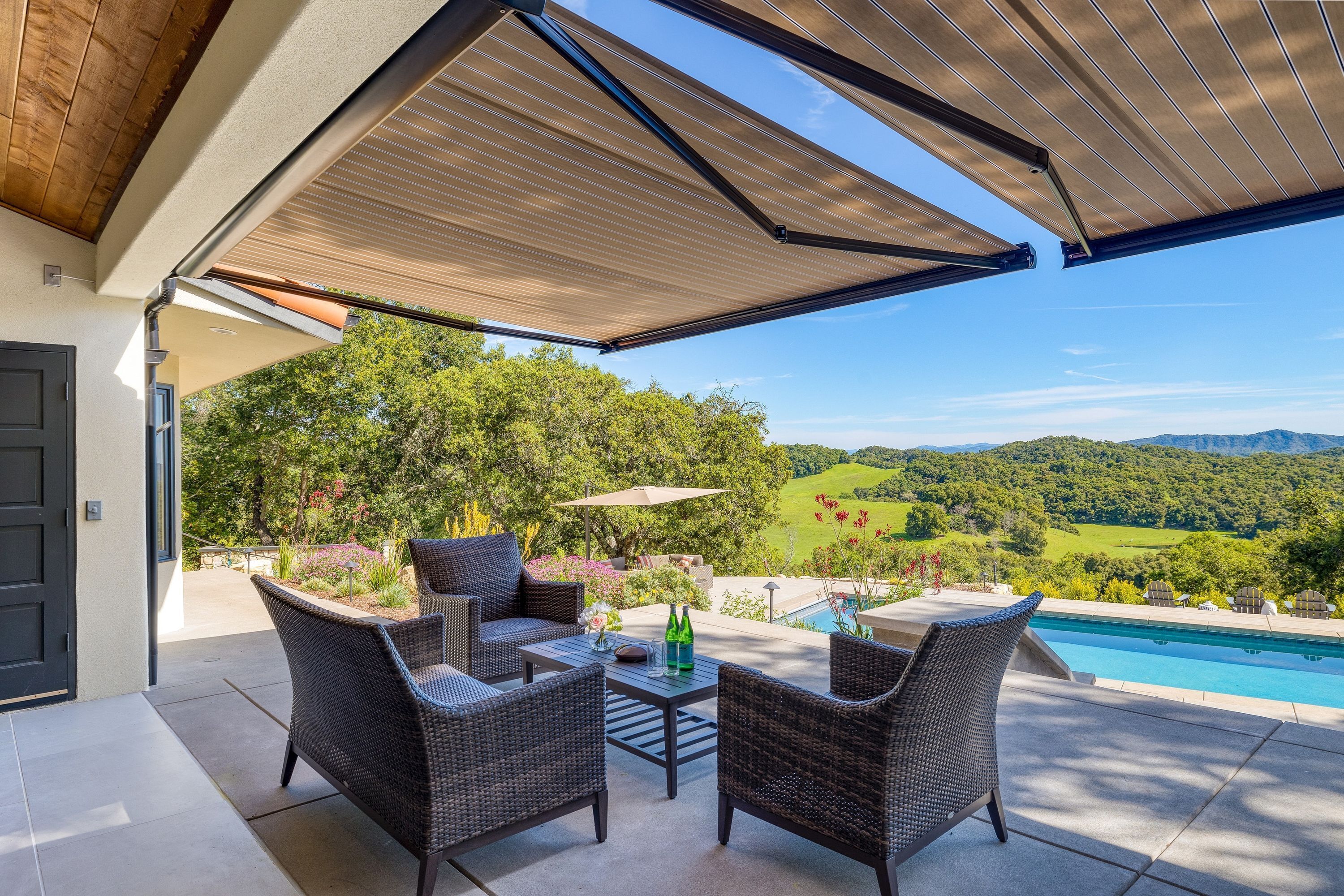 An outdoor patio with wicker furniture, a pool, and a scenic view of hills and greenery.