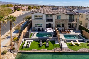 A multi-story house with a large backyard featuring two swimming pools, a patio with outdoor furniture, and a well-maintained lawn. - Lago Luxe by Avantstay Lakefront Private Pool Great for Festival Season (Indio)