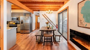 A wooden ceiling, a dining table with benches, a kitchen area, and a fireplace.