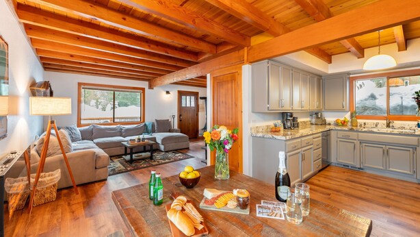 A spacious living room with a wooden ceiling, a kitchen with grey cabinets, and a dining area with a table set for a meal.
