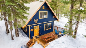 A cabin with a wooden deck, a front door, and a window.