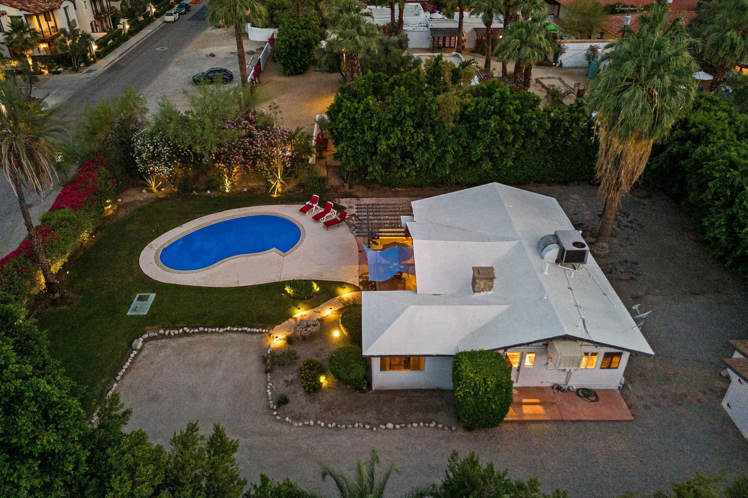 Eine Vogelperspektive zeigt ein Haus mit Swimmingpool, einer Terrasse mit Stühlen und einem gepflegten Garten.