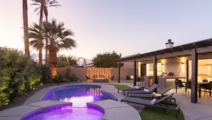 En have med jacuzzi, liggestole og en patio med spisebord og stole.