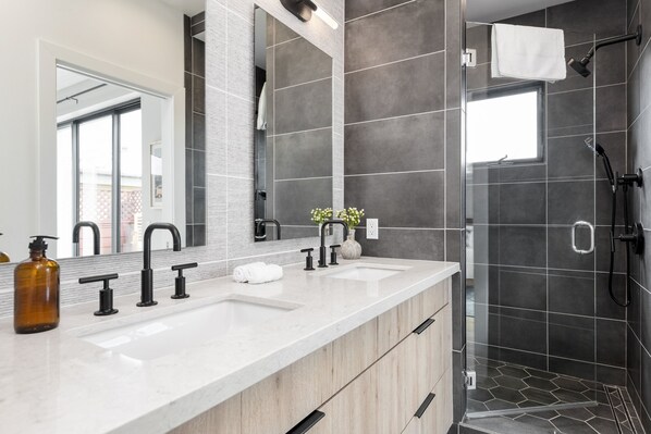 Un baño moderno con un espejo grande, dos lavamanos, zona de ducha y una ventana que proporciona luz natural.