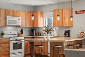 Una cocina moderna con armarios de madera, una isla central con taburetes, un microondas, una estufa y una cafetera.