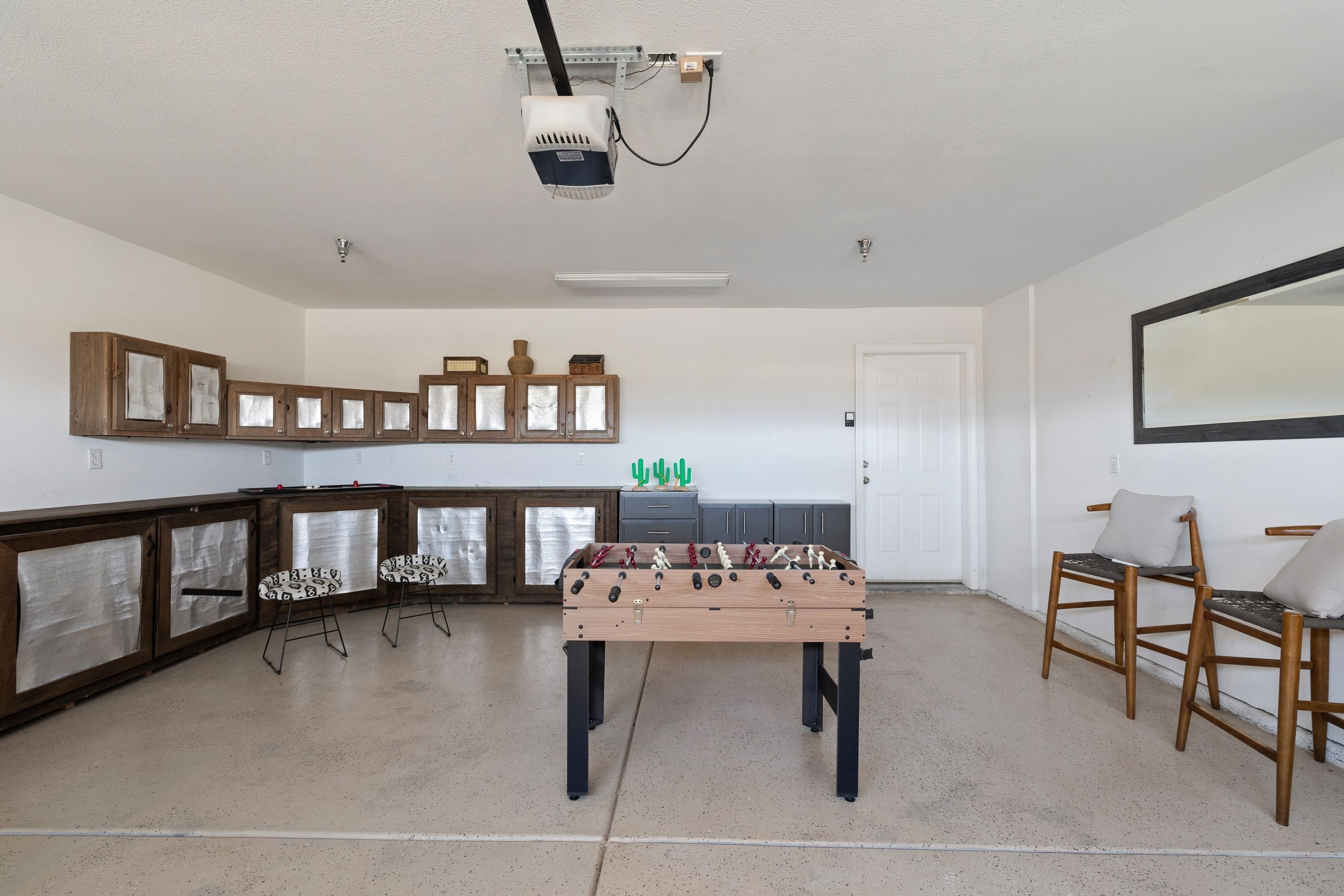 A room with a foosball table, wooden cabinets, and a projector mounted on the ceiling.
