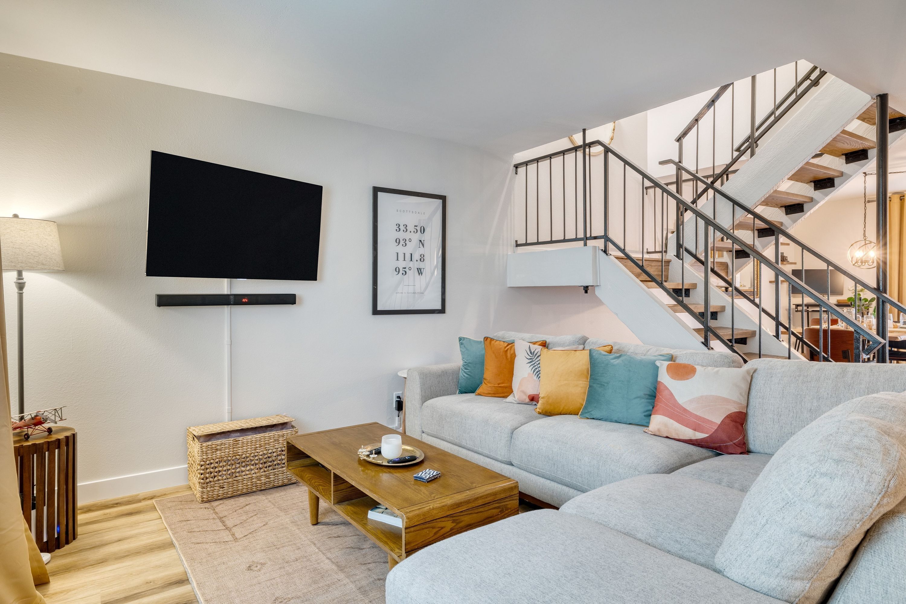 A modern living room with a grey sofa, a wooden coffee table, a flat-screen TV, and a staircase leading to an upper level.