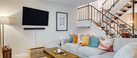 A modern living room with a grey sofa, a wooden coffee table, a flat-screen TV, and a staircase leading to an upper level.