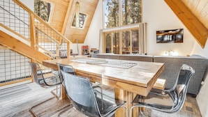 A spacious dining area with a wooden table and chairs, a staircase, and a large window with a view of trees.