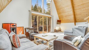 A spacious living area with a high ceiling and large windows offering a view of trees. There is a sofa, a coffee table, and a chair.