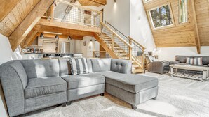 A spacious loft with a large gray sectional sofa, wooden beams, and a mezzanine with a staircase.
