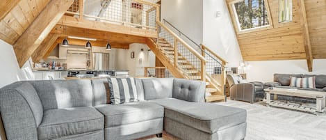 A spacious loft with a large gray sectional sofa, wooden beams, and a mezzanine with a staircase.