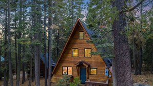 A wooden cabin with a triangular roof, surrounded by tall pine trees.
