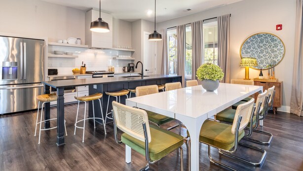 A modern kitchen with a central island, stainless steel appliances, and a dining area with a white table and green cushioned chairs. - The Magnolia 10 - Avantstay Germantown w Private Balcony (Nashville)