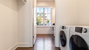 A laundry room with two front-loading washing machines, a window with a view of the outside, and a wooden floor. - The Magnolia 10 - Avantstay Germantown w Private Balcony (Nashville)
