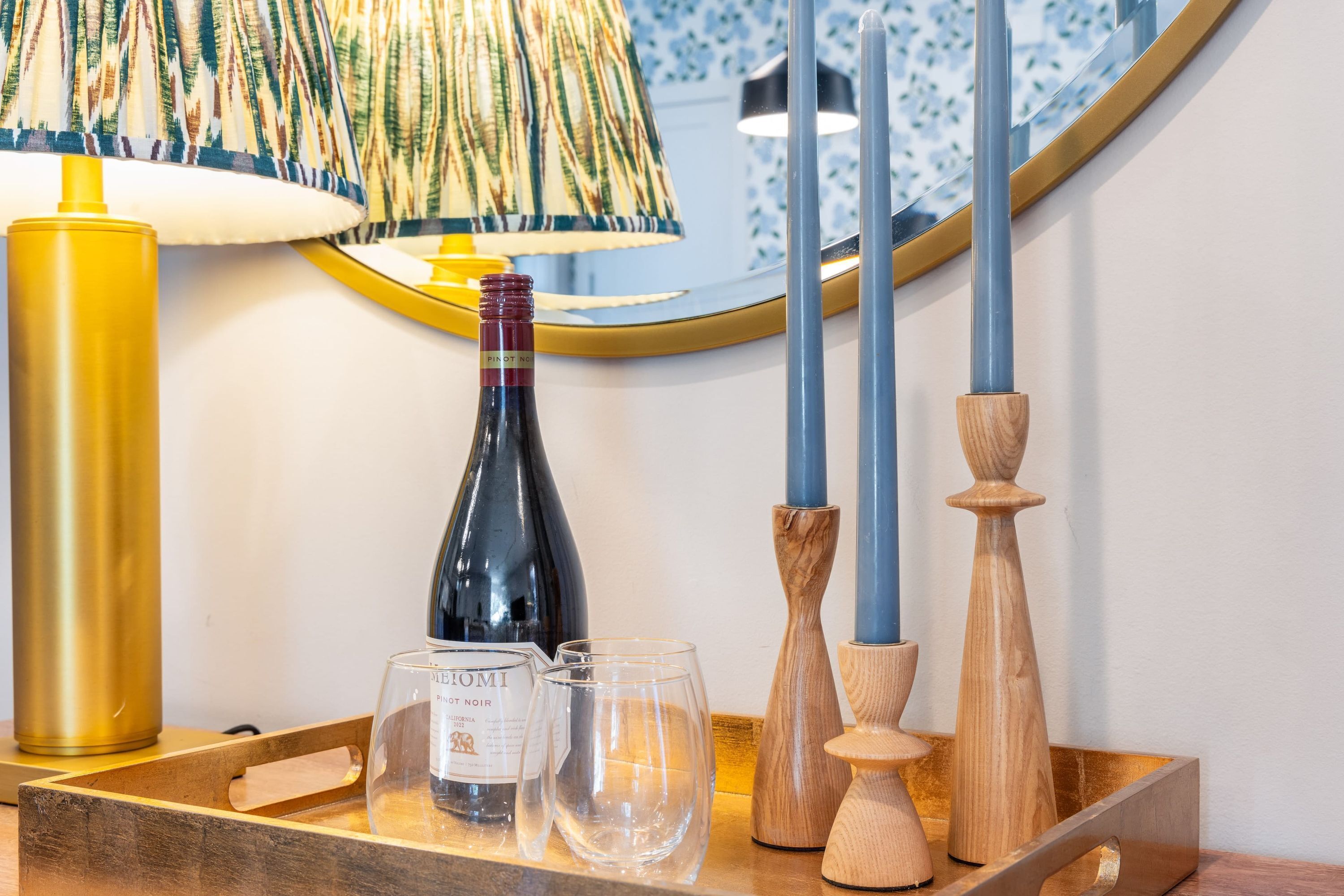 A wooden tray with a bottle of wine, two glasses, and candle holders on a table.