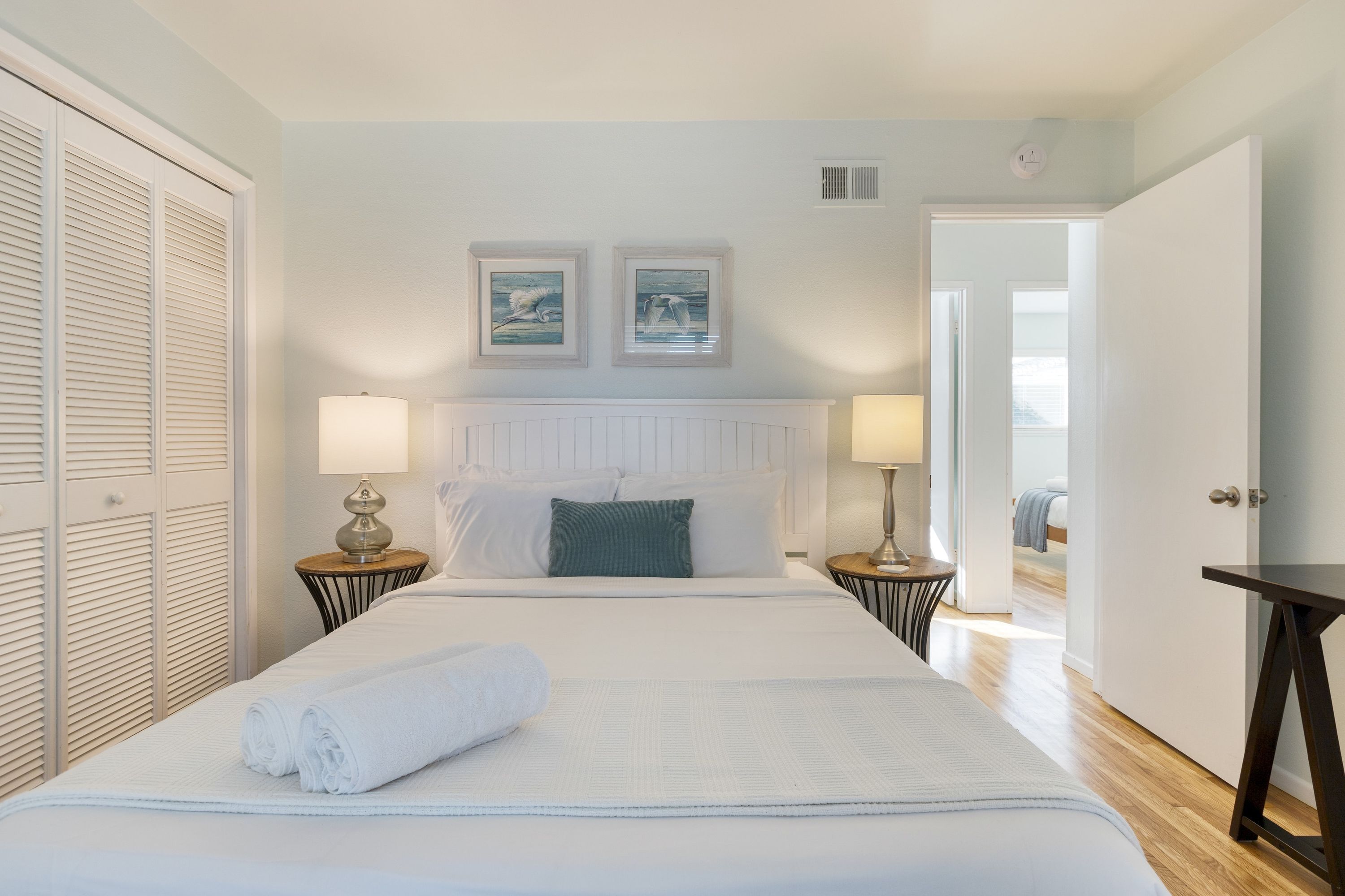 A neatly made bed with white linens and a rolled towel, flanked by two bedside tables with lamps.