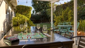 Eine Terrasse mit Tisch für zwei Personen, ausgestattet mit einem Gesellschaftsspiel, zwei Weingläsern und einer Brieftasche.