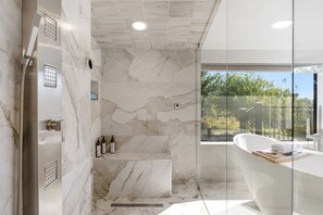 Un baño moderno con una bañera independiente, ducha con múltiples cabezales y zona de ducha con mampara de vidrio.