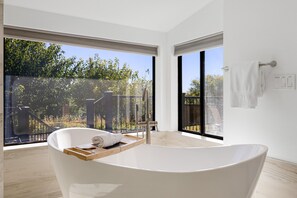 Un baño moderno con una bañera independiente, ventanas amplias y vistas a un jardín.