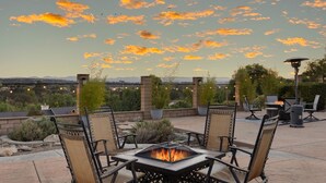 An outdoor patio with a fire pit table, chairs, and a view of the cityscape.