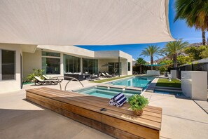Uma área de piscina moderna ao ar livre, com deck de madeira, espreguiçadeiras e um grande guarda-sol.