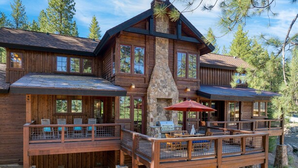 A two-story log cabin with a stone chimney, outdoor dining area, and a deck with a railing. - Grays Crossing by Avantstay Stunning 4bdr Cabin (Truckee)