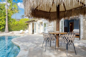 A poolside area with a thatched umbrella, lounge chairs, and a dining table. - Wavebreak by Avantstay Close to Beaches Surfing (Solana Beach)