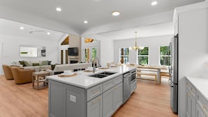 A modern kitchen with grey cabinetry, a large island, and a dining area with a view of greenery.