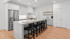 A modern kitchen with white cabinetry, a stainless steel refrigerator, a central island with bar stools, and recessed ceiling lighting.