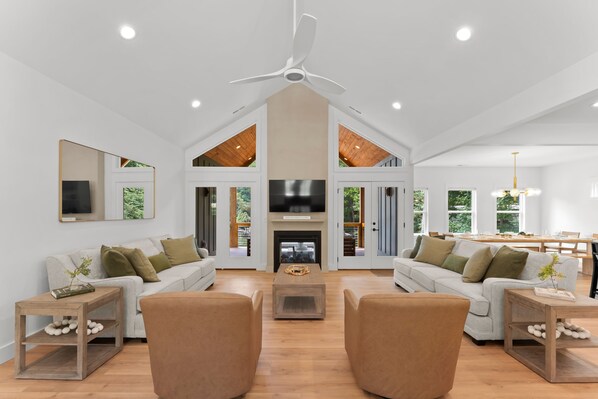 A spacious living room with a high ceiling, a fireplace, and a large TV. - Hideaway Cove Private Dock Firepit New Build (Mooresville)