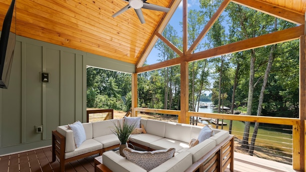 A covered outdoor seating area with a wooden ceiling and large windows overlooking a lake.