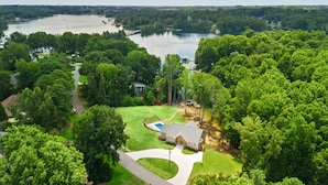 An aerial view of a residential area with a large lake, surrounded by dense greenery and a house with a swimming pool.