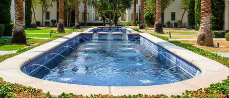 A rectangular pool with a tiled edge, surrounded by a low hedge and palm trees.