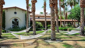 A courtyard with palm trees, a white building with a red-tiled roof, and two hammocks.