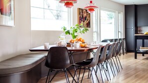 A modern dining area with a long table, multiple chairs, and pendant lights.