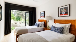 A hotel room with two beds, a ceiling fan, a window with curtains, and artwork on the walls.