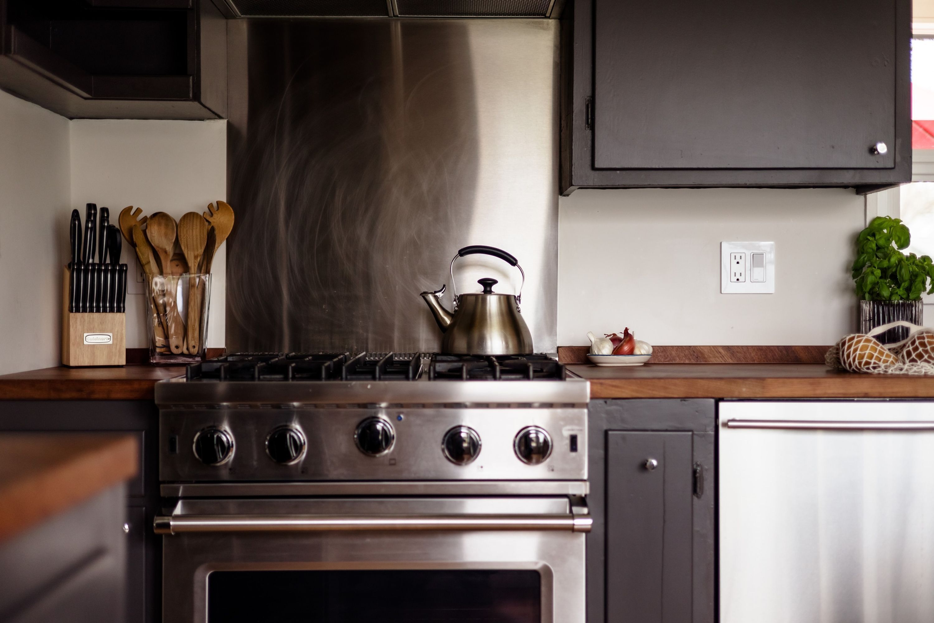 A kitchen with a stainless steel stove, a kettle, and a wooden utensil holder.